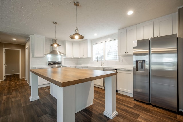 kitchen with stainless steel appliances, white cabinetry, hanging light fixtures, and butcher block counters