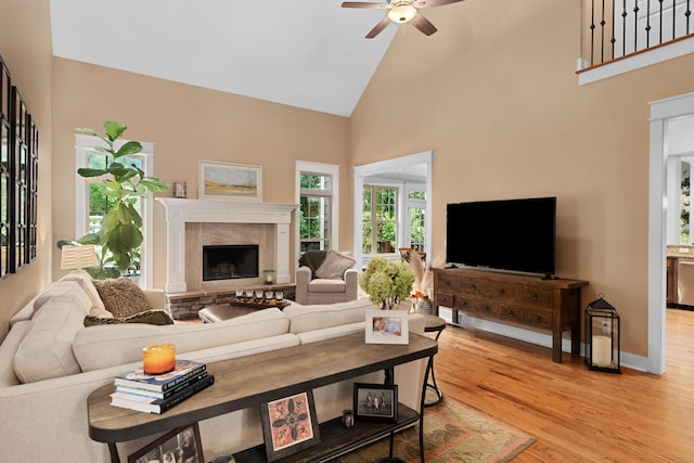 living room featuring a tiled fireplace, ceiling fan, high vaulted ceiling, and light hardwood / wood-style floors