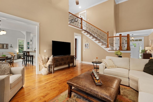 living room with crown molding, ceiling fan, wood-type flooring, and a high ceiling