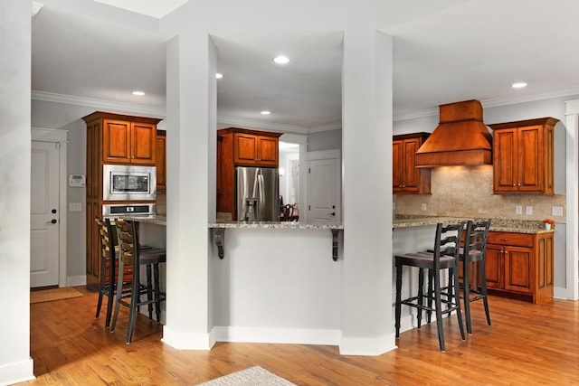 kitchen with a breakfast bar area, tasteful backsplash, light hardwood / wood-style flooring, custom range hood, and stainless steel appliances