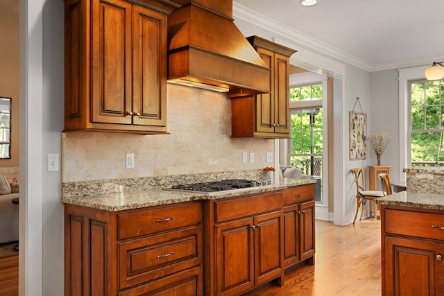 kitchen featuring crown molding, backsplash, light stone counters, stainless steel gas cooktop, and custom exhaust hood