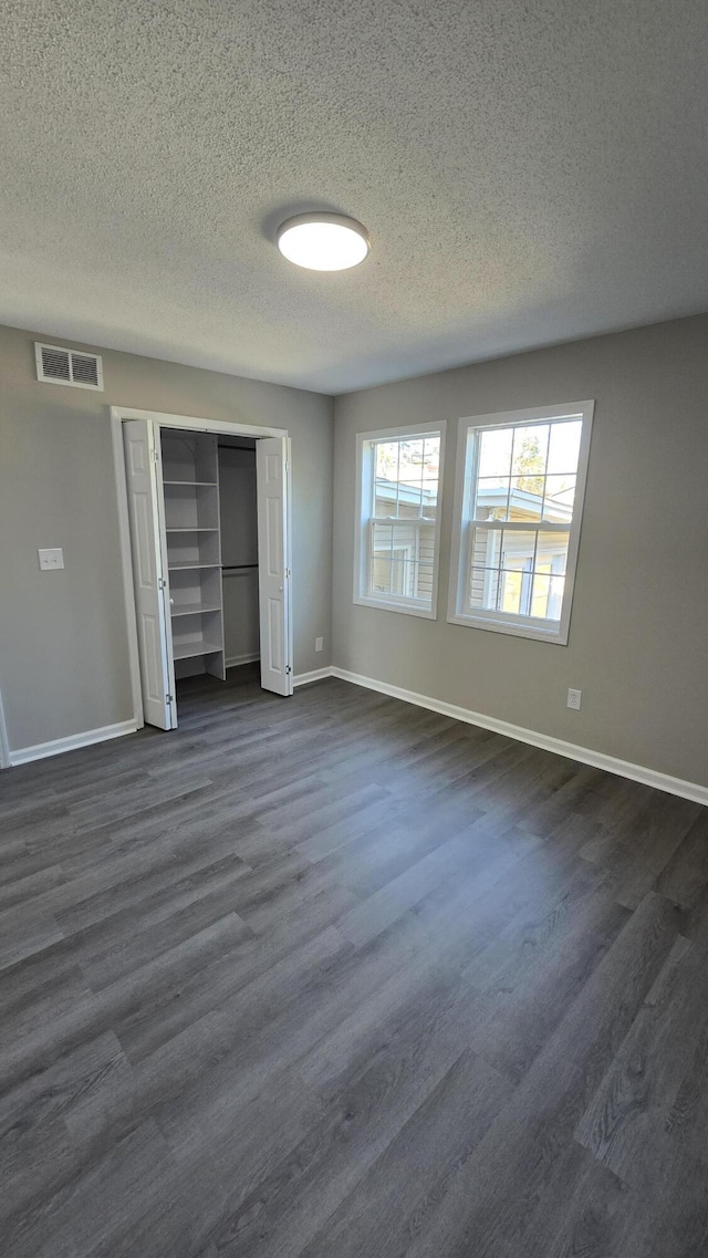 unfurnished bedroom featuring dark wood-type flooring, a textured ceiling, and a closet