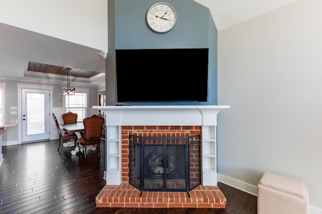 living room with a brick fireplace, wood-type flooring, ornamental molding, and a raised ceiling