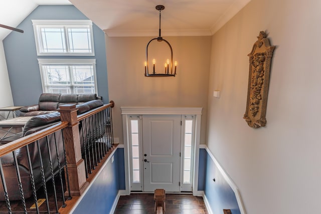 entryway featuring crown molding, lofted ceiling, dark wood-type flooring, and a notable chandelier