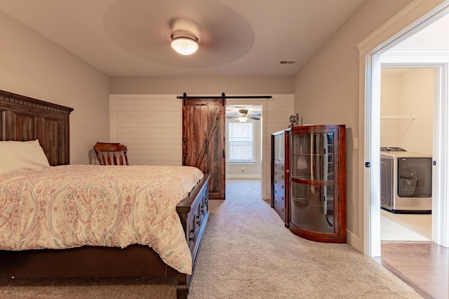 bedroom featuring washer and dryer, ceiling fan, a barn door, and light carpet