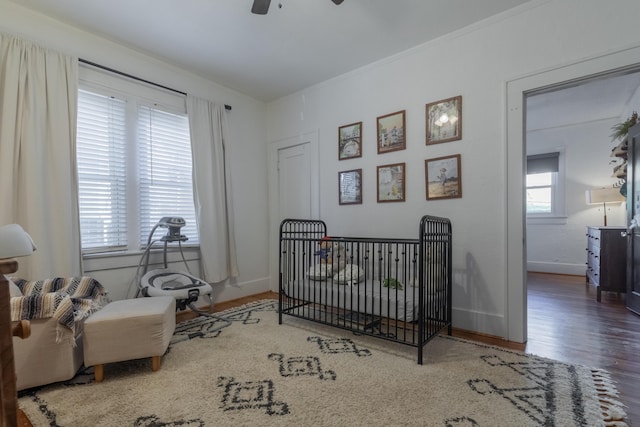 bedroom with ornamental molding, a nursery area, hardwood / wood-style floors, and ceiling fan