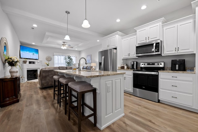 kitchen with light stone counters, white cabinetry, stainless steel appliances, and a kitchen island with sink