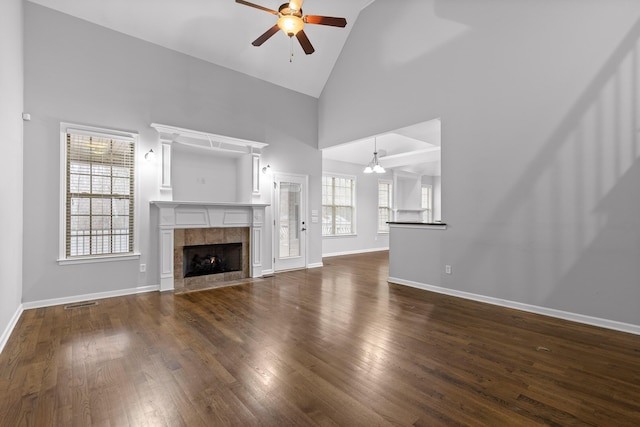 unfurnished living room with a tiled fireplace, ceiling fan, dark wood-type flooring, and a healthy amount of sunlight