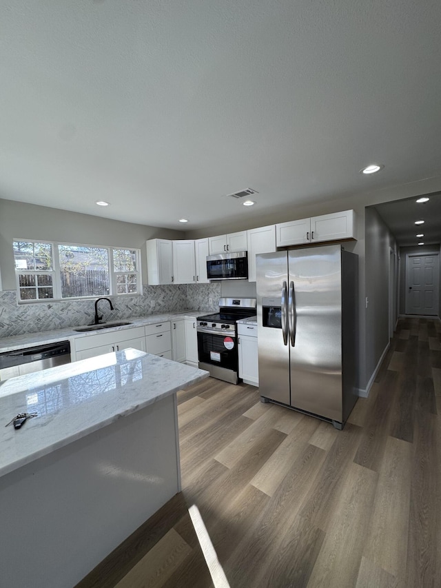 kitchen featuring sink, wood-type flooring, stainless steel appliances, light stone countertops, and white cabinets