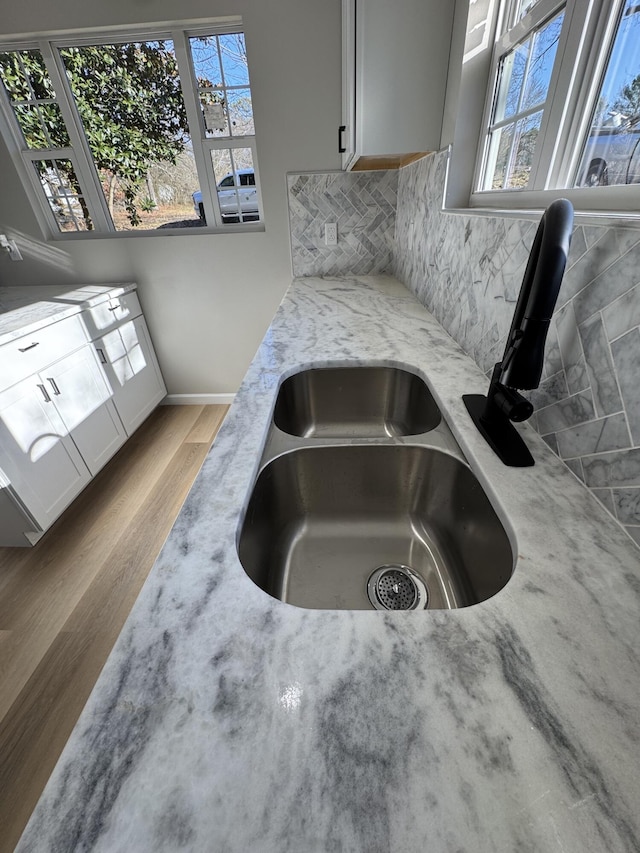 kitchen with tasteful backsplash, sink, white cabinets, light stone counters, and light wood-type flooring