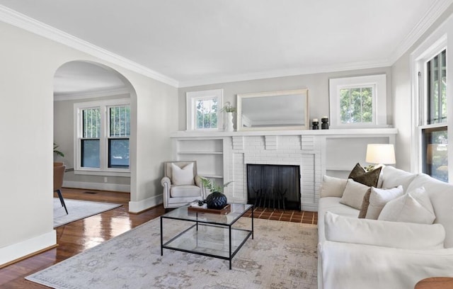 living room featuring a brick fireplace, wood-type flooring, and ornamental molding