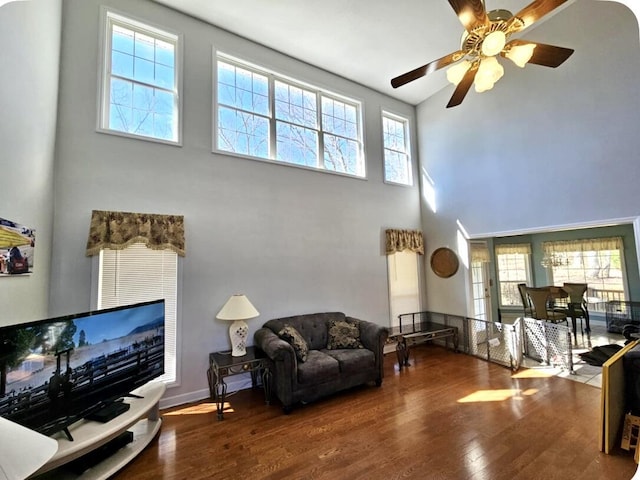 living room with hardwood / wood-style flooring, ceiling fan, a towering ceiling, and a wealth of natural light