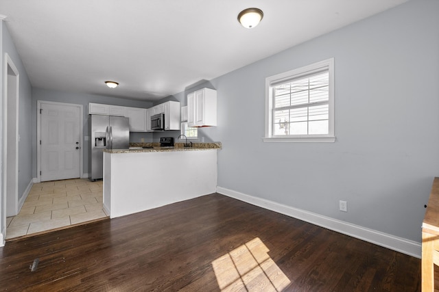 kitchen featuring wood-type flooring, appliances with stainless steel finishes, white cabinets, and kitchen peninsula