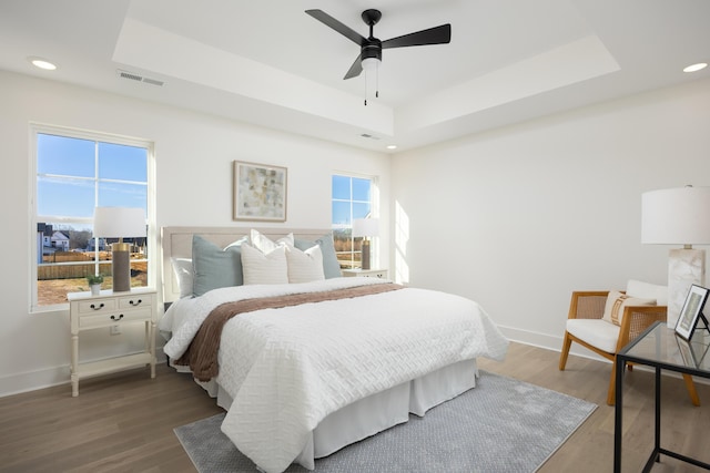 bedroom with ceiling fan, wood-type flooring, and a raised ceiling