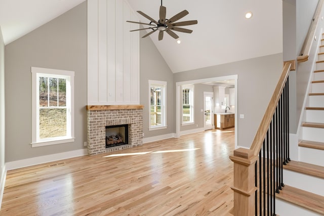 unfurnished living room with light wood-style flooring, stairs, a fireplace, high vaulted ceiling, and a sink