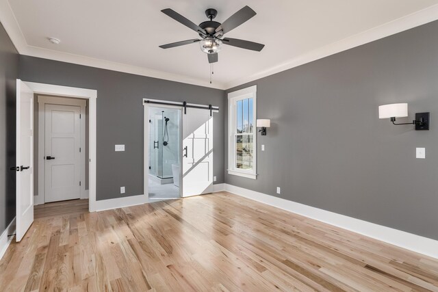 foyer entrance featuring light wood-style flooring, a barn door, ornamental molding, a ceiling fan, and baseboards