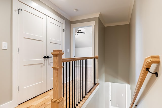 hall with light wood-type flooring, crown molding, and an upstairs landing