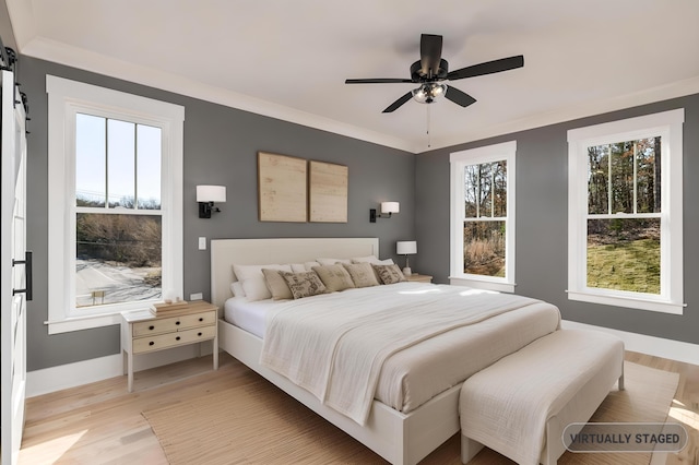 bedroom with light wood finished floors, a barn door, multiple windows, and ornamental molding