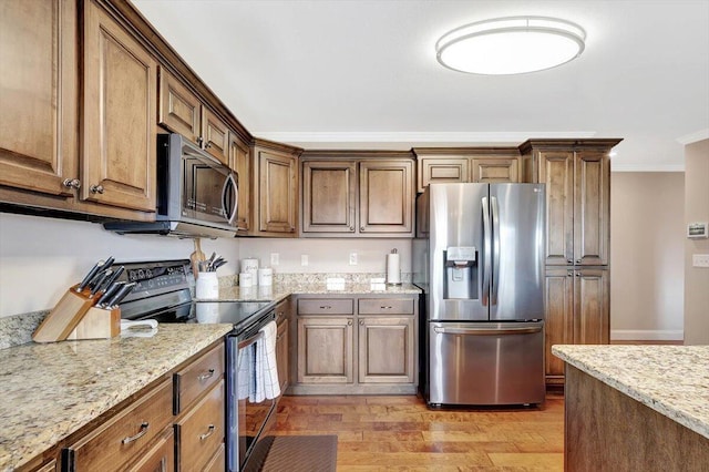 kitchen featuring ornamental molding, stainless steel appliances, light stone countertops, and light wood-type flooring