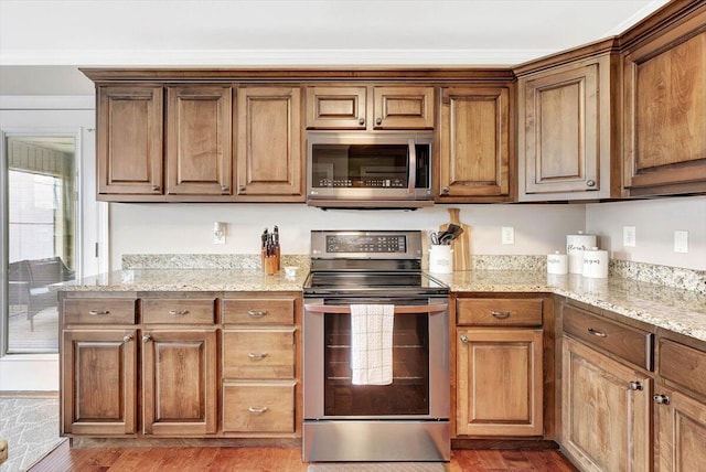 kitchen with stainless steel appliances, hardwood / wood-style flooring, and light stone counters