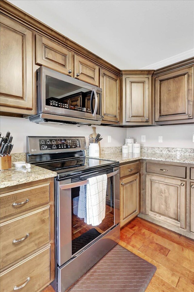 kitchen with stainless steel appliances, light stone countertops, and light hardwood / wood-style floors