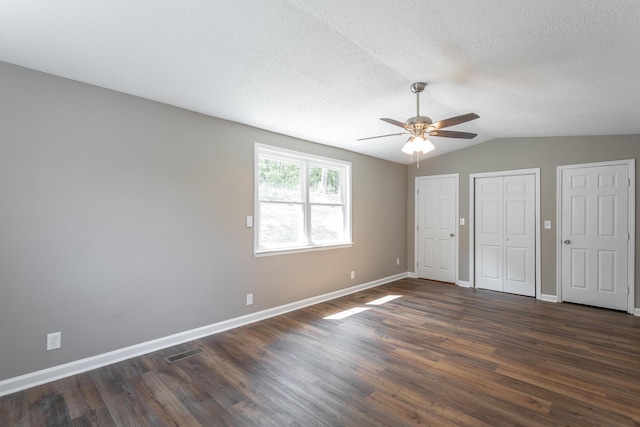 unfurnished bedroom with dark wood-type flooring, vaulted ceiling, a textured ceiling, and two closets