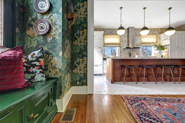 bar with decorative light fixtures, hardwood / wood-style floors, and wall chimney range hood