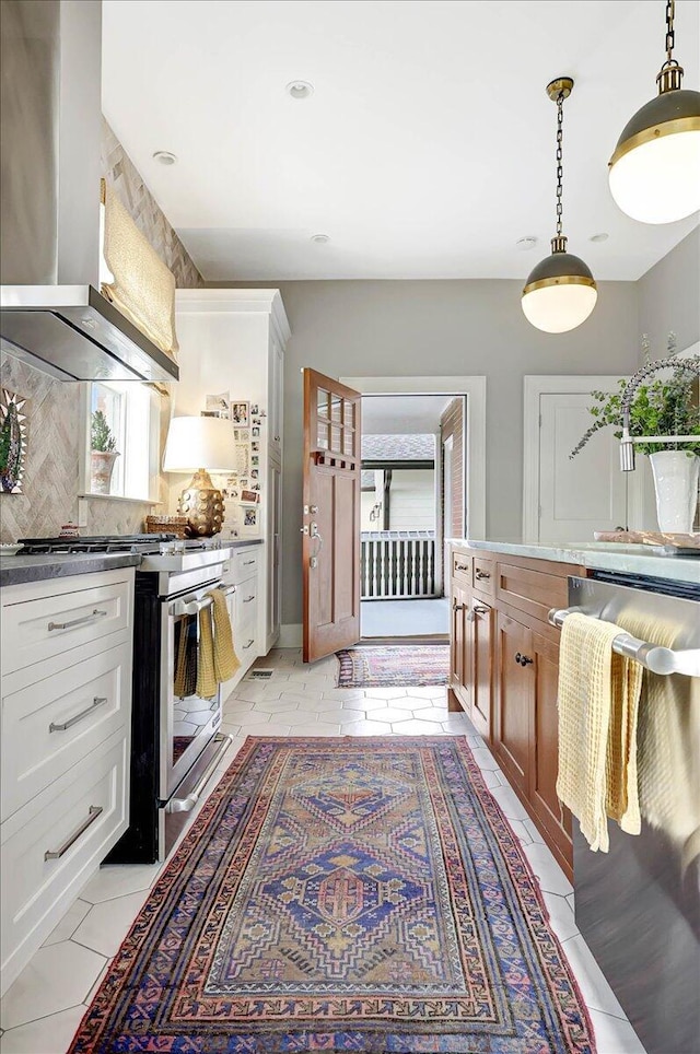 kitchen featuring wall chimney range hood, stainless steel gas range oven, dishwasher, and white cabinets