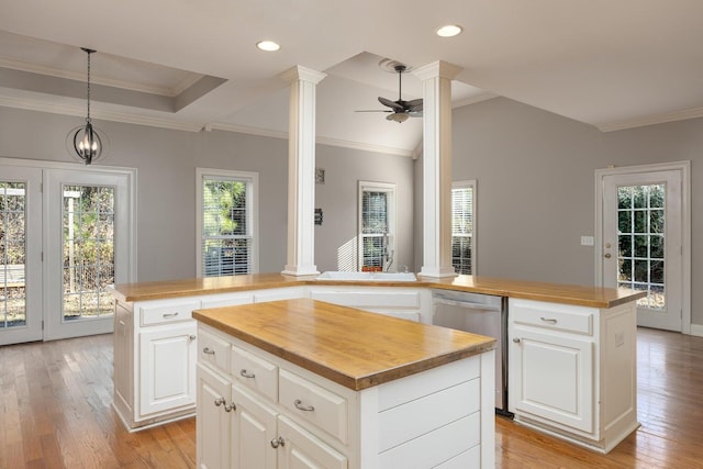 kitchen featuring butcher block counters, hanging light fixtures, a center island, and ornate columns