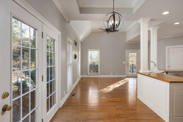 unfurnished dining area featuring sink, crown molding, an inviting chandelier, decorative columns, and wood-type flooring