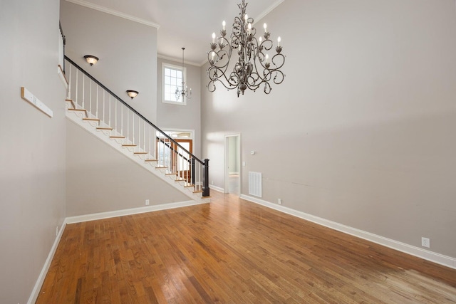 interior space with a notable chandelier, hardwood / wood-style flooring, ornamental molding, and a towering ceiling