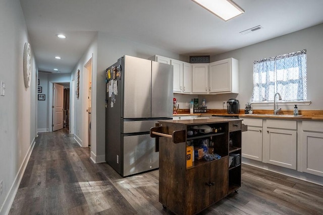 kitchen with dark wood-type flooring, sink, stainless steel fridge, a kitchen island, and white cabinets