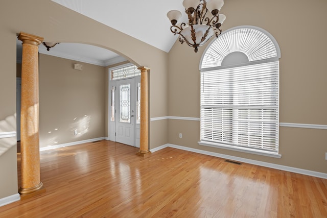 entryway featuring lofted ceiling, wood-type flooring, a notable chandelier, crown molding, and ornate columns