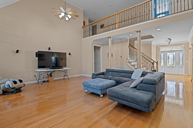 living room with light hardwood / wood-style flooring, a towering ceiling, ceiling fan, ornate columns, and ornamental molding