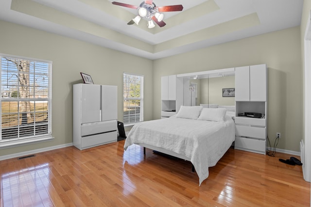 bedroom with light wood-type flooring, a tray ceiling, and ceiling fan