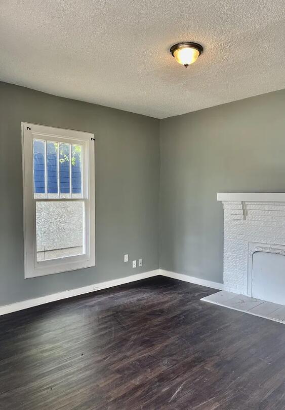 unfurnished living room with dark wood-type flooring, a textured ceiling, and a fireplace