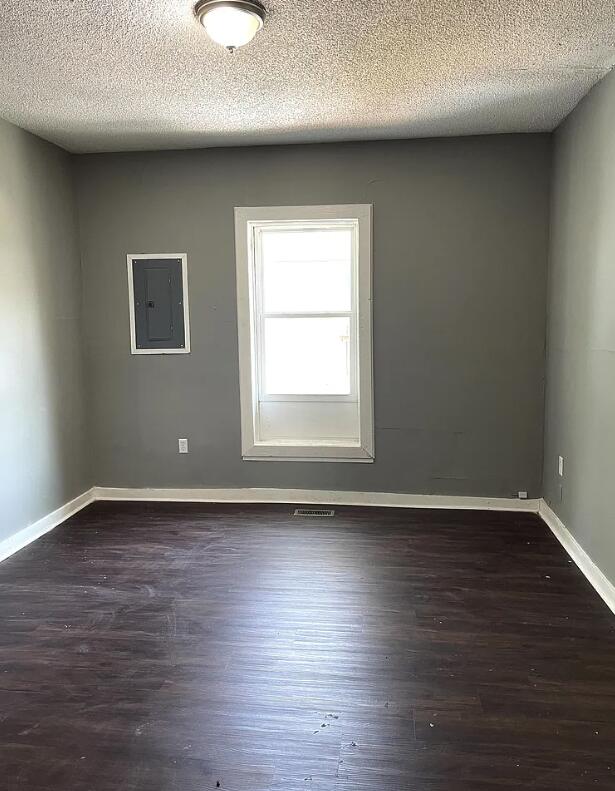 empty room with dark wood-type flooring, electric panel, and a textured ceiling