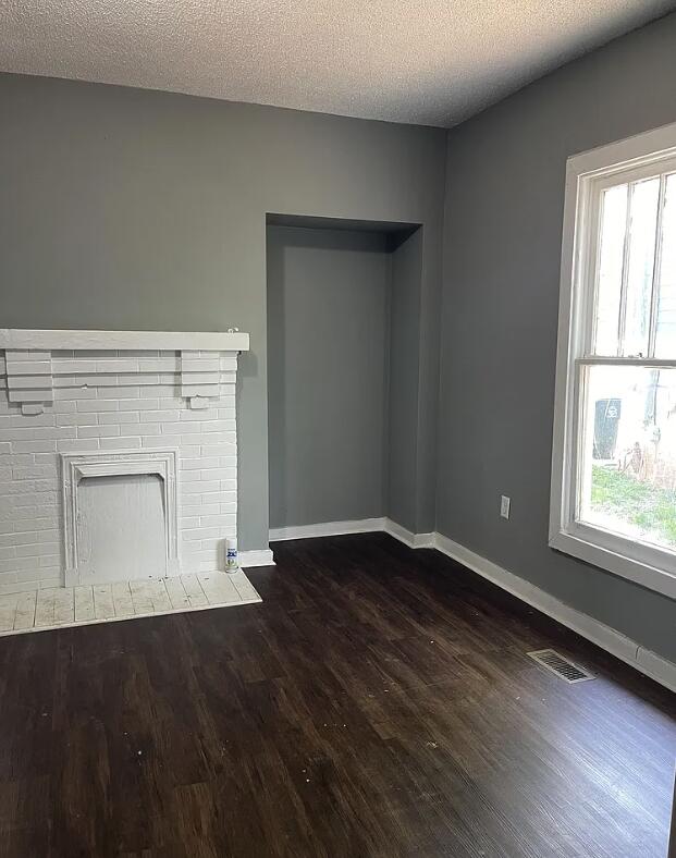 unfurnished living room featuring dark wood-type flooring, a textured ceiling, and plenty of natural light