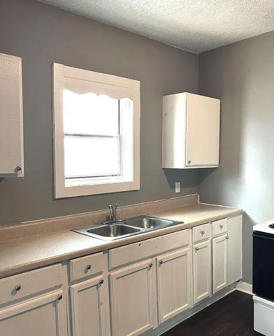 kitchen with range with electric cooktop, dark hardwood / wood-style floors, white cabinetry, sink, and a textured ceiling