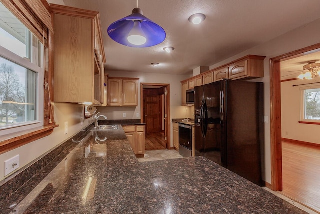 kitchen featuring appliances with stainless steel finishes, sink, dark stone countertops, hanging light fixtures, and light brown cabinets