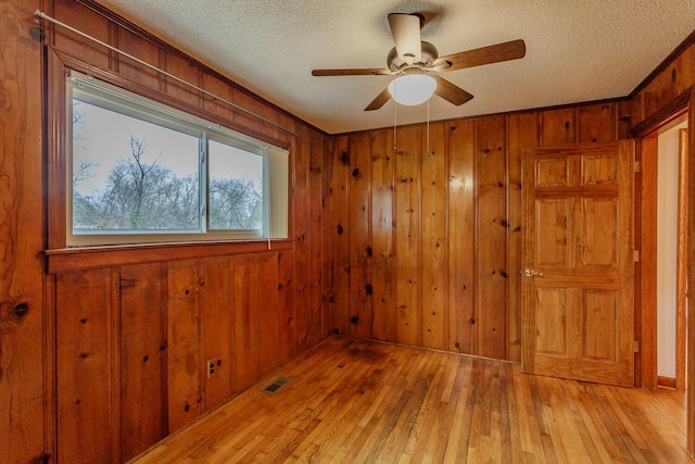 spare room featuring wooden walls, light hardwood / wood-style floors, and a textured ceiling