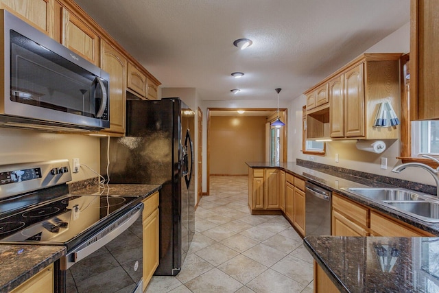 kitchen featuring sink, light tile patterned floors, appliances with stainless steel finishes, dark stone countertops, and decorative light fixtures