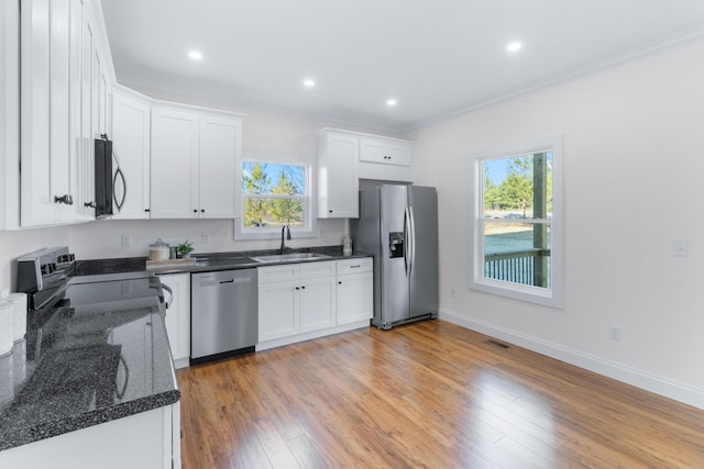 kitchen with sink, appliances with stainless steel finishes, light hardwood / wood-style floors, white cabinets, and dark stone counters