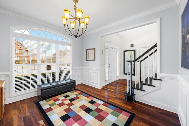 entrance foyer with a chandelier, a wainscoted wall, wood finished floors, stairs, and ornamental molding