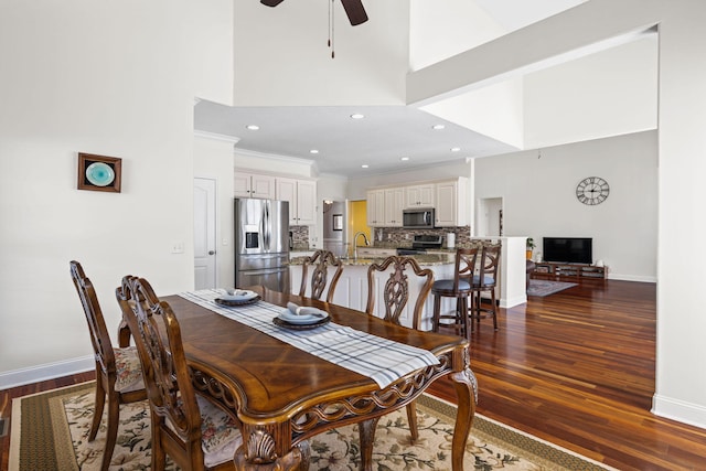 dining area featuring dark wood-type flooring, a high ceiling, crown molding, and baseboards