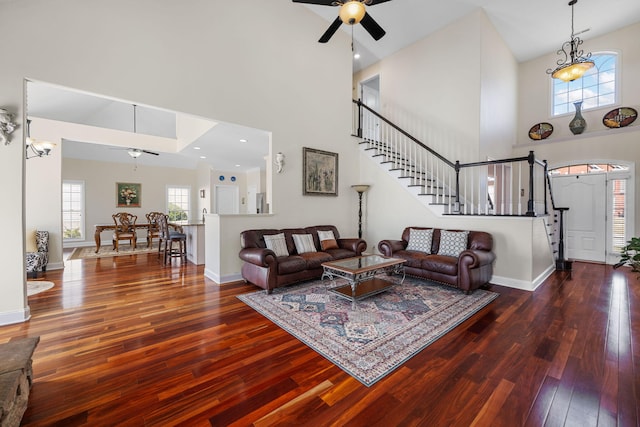 living area featuring a towering ceiling, hardwood / wood-style floors, ceiling fan, baseboards, and stairs