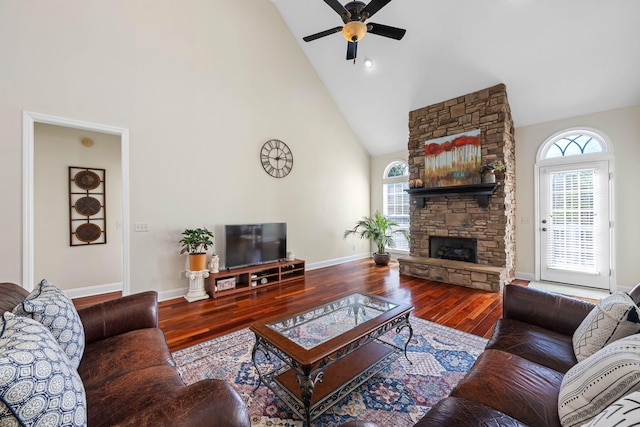 living area with baseboards, high vaulted ceiling, wood finished floors, and a stone fireplace