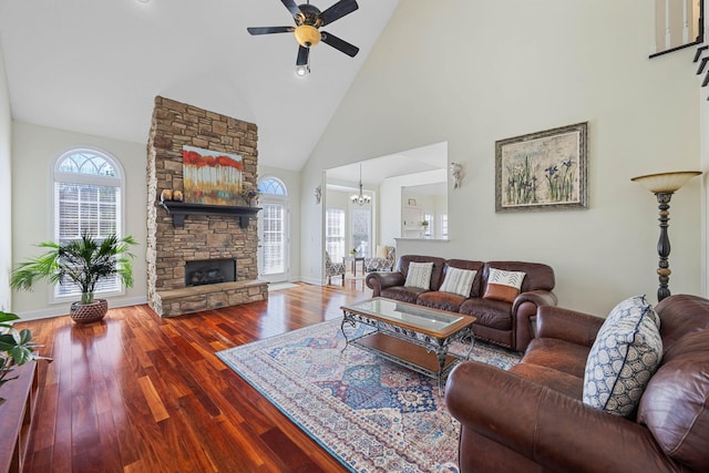 living area with a stone fireplace, wood finished floors, high vaulted ceiling, baseboards, and ceiling fan with notable chandelier