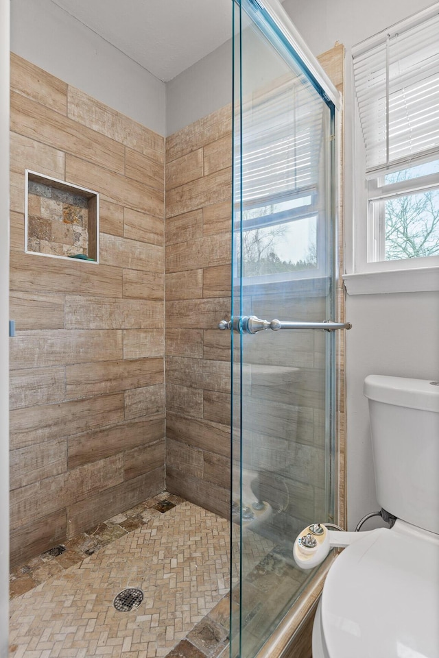 bathroom featuring a shower with door and toilet