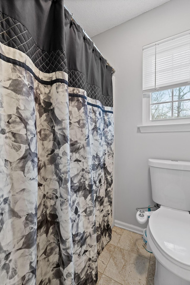 bathroom featuring a shower with curtain, toilet, and a textured ceiling